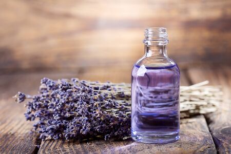 glass bottle of lavender essential oil with dried flowers on wooden tableの写真素材