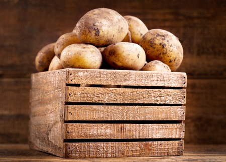 fresh raw potatoes in a wooden box on wooden backgroundの写真素材