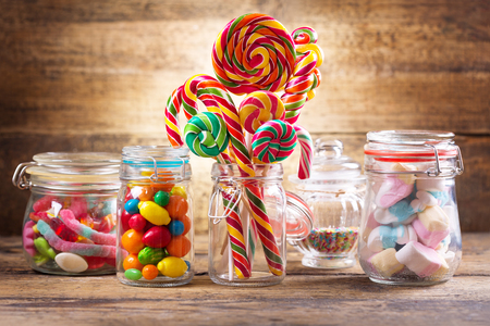 Colorful candies, jellies, lollipops, marshmallows and marmalade in a glass jars on wooden tableの写真素材
