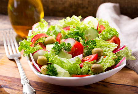 bowl of fresh salad with vegetables and greens on wooden boardの写真素材