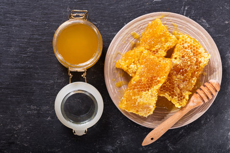 honeycombs and jar of honey on dark background, top view