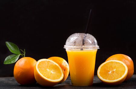 orange juice in takeaway plastic cup with fresh fruits on dark tableの写真素材