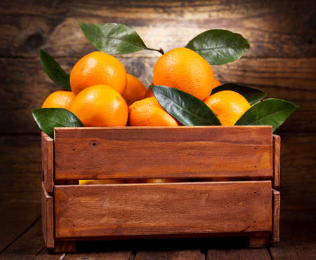 fresh orange fruits with leaves in a box on wooden tableの写真素材