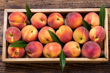 fresh peaches with leaves in a wooden box, top viewの写真素材