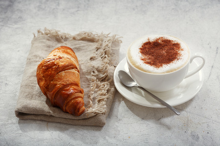 Cup of cappuccino coffee with croissant on old tableの写真素材