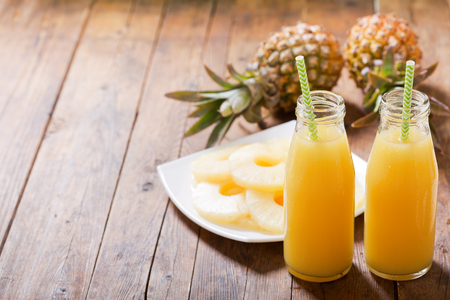 bottles of pineapple juice with fresh fruits on wooden tableの写真素材
