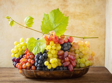 mix of fresh ripe grapes with leaves in a bowl on a wooden table