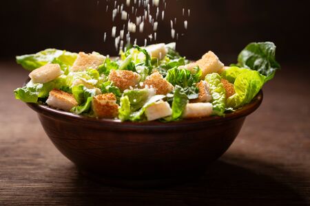 Falling cheese into Bowl of fresh caesar salad on a wooden tableの写真素材