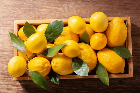 Fresh lemons with leaves in a wooden box, top viewの写真素材