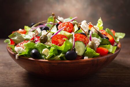 bowl of fresh salad with vegetables, feta cheese and capers on a wooden tableの写真素材
