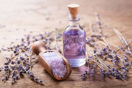 Glass bottle of lavender essential oil and purple bath salt with dried lavender flowers on a wooden tableの写真素材