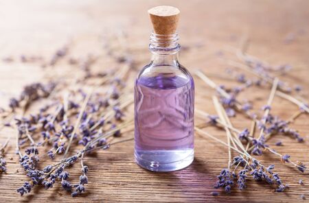 Glass bottle of lavender essential oil with dried lavender flowers on wooden tableの写真素材