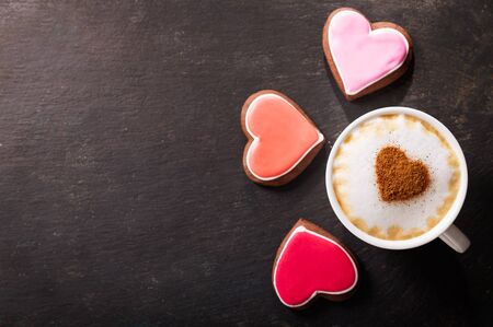 Valentines day.  Cup of cappuccino coffee with drawn heart and colorful heart shaped cookies on dark background, top viewの写真素材