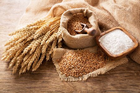 Wheat ears, grains and bowl of flour on a wooden table, top viewの写真素材