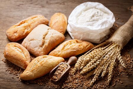 fresh bread with wheat ears, flour and grains on a wooden tableの写真素材