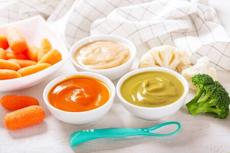 Baby food. Various kinds of bowls of vegetable puree with ingredients for cooking on a wooden tableの写真素材