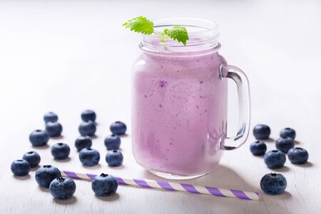 glass jar of blueberry smoothie with fresh berries on a wooden tableの写真素材