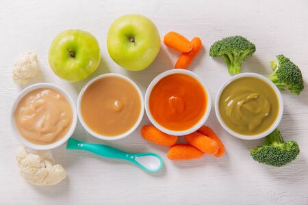 Baby food. Various kinds of bowls of fruit and vegetable puree with ingredients for cooking on a wooden table, top viewの写真素材