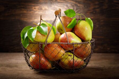 fresh pears with leaves in a basket on a wooden tableの写真素材