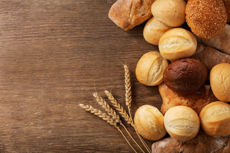 Fresh baked bread and wheat ears on a wooden table, top view