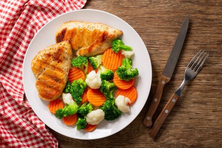 A plate of grilled chicken with vegetables on a wooden table, top viewの写真素材