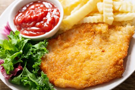A plate of fried breaded chicken meat or Schnitzel with french fries and salad on wooden tableの写真素材