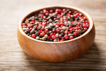 A bowl of various peppercorns on a wooden tableの写真素材