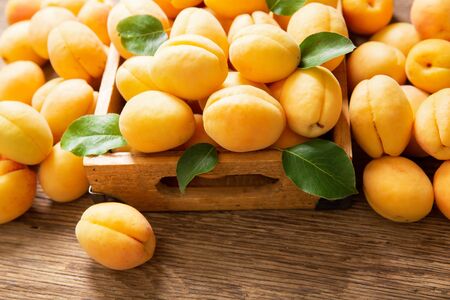 fresh ripe apricots with leaves in a box on a wooden tableの写真素材