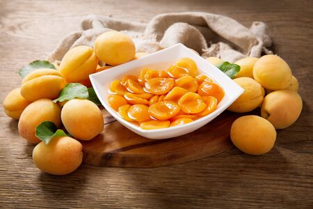 bowl of canned apricots and fresh fruits on wooden table, top viewの写真素材