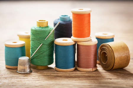 sewing tools: bobbins with thread and needles on wooden tableの写真素材