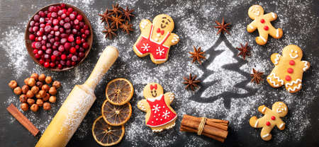 Christmas food. Ingredients for Christmas baking: fir tree made from flour, kitchen utensils, frozen cranberries and gingerbread cookies on a dark table, top viewの写真素材