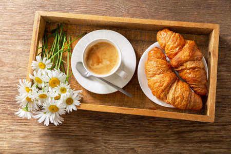 cup of coffee, croissants and daisy flowers on a wooden tray, top viewの写真素材