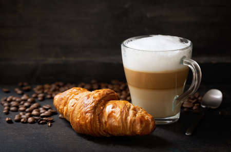glass of latte macchiato coffee and croissant on a dark backgroundの写真素材