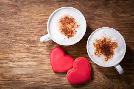 Valentines day. Cups of cappuccino coffee and colorful heart shaped cookies on wooden background, top viewの写真素材