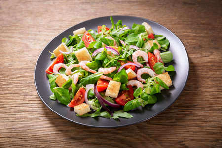 plate of fresh salad with shrimps, greens and tomato on a wooden table, top viewの写真素材