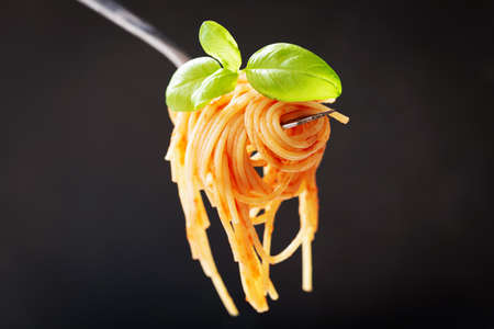 pasta with tomato sauce and green basil on a fork on dark backgroundの写真素材