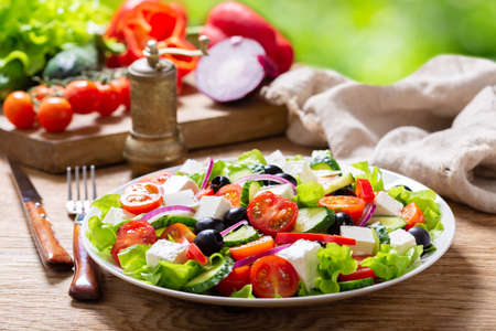 Plate of fresh salad with vegetables, feta cheese and olives on a wooden table. Greek salad.の写真素材