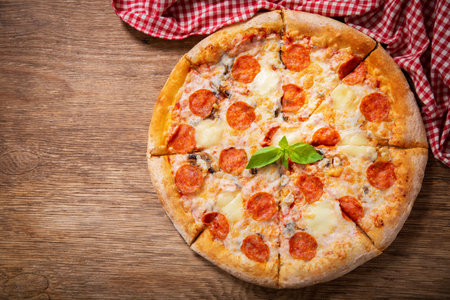 pizza with mozzarella cheese and pepperoni on a wooden table, top viewの写真素材