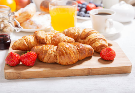 Breakfast with croissants, coffee, juice, jam, cereals and fresh fruits on a wooden tableの写真素材