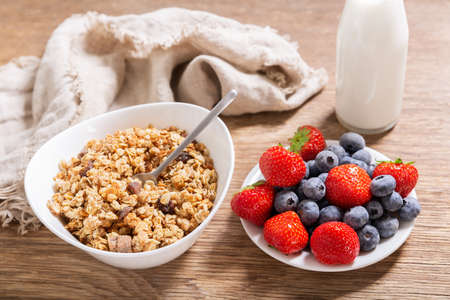 breakfast with bowl of granola, fresh berries and bottle of milk on a wooden tableの写真素材