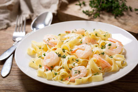 plate of pasta fettuccine with cream sauce and shrimps on a wooden tableの写真素材