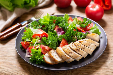 plate of chicken salad with vegetables on wooden tableの写真素材