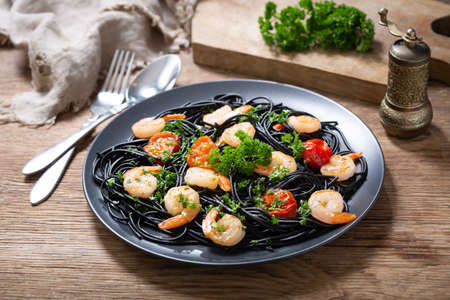 plate of black pasta with shrimps and vegetables on a wooden tableの写真素材