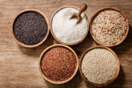 Various types of rice: white, brown, mix grain, black rice and red in a bowls on a wooden background, top viewの写真素材