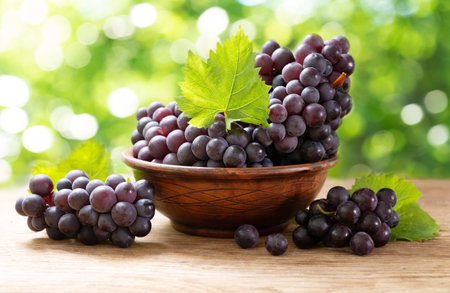 fresh ripe grapes with leaves in a bowl on a wooden tableの写真素材