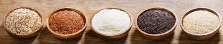 Various types of rice: white, brown, mix grain, black rice and red in a bowls on a wooden backgroundの写真素材