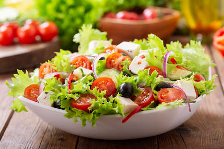 Bowl of fresh salad with vegetables, feta cheese and olives on a wooden table. Greek salad.の写真素材
