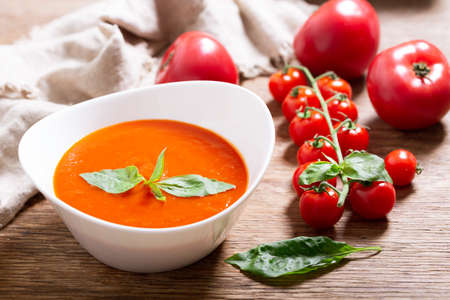 plate of tomato soup with basil on wooden tableの写真素材