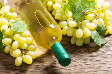Bottle of white wine and green grapes on a wooden tableの写真素材