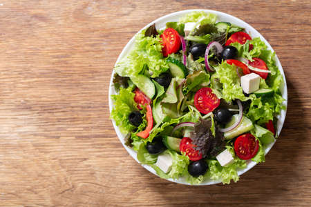 Plate of fresh salad with vegetables, feta cheese and olives on wooden background, top viewの写真素材